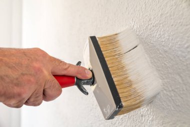 Bir ele yakın çekim. Bir ressam boya fırçasını kullanarak duvarları beyaz boyayla boyar. İnşaat endüstrisi. 
