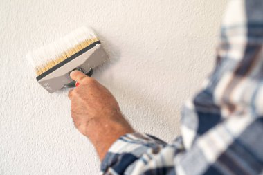 Bir ele yakın çekim. Bir ressam boya fırçasını kullanarak duvarları beyaz boyayla boyar. İnşaat endüstrisi. 