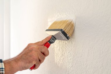 Bir ele yakın çekim. Bir ressam boya fırçasını kullanarak duvarları beyaz boyayla boyar. İnşaat endüstrisi. 