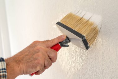 Bir ele yakın çekim. Bir ressam boya fırçasını kullanarak duvarları beyaz boyayla boyar. İnşaat endüstrisi. 