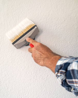 Bir ele yakın çekim. Bir ressam boya fırçasını kullanarak duvarları beyaz boyayla boyar. İnşaat endüstrisi. 