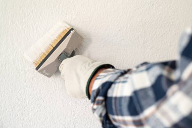 Koruyucu eldiven takan ellerin yakın çekimi. Bir ressam boya fırçasını kullanarak duvarları beyaz boyayla boyar. İnşaat endüstrisi. İş Güvenliği.
