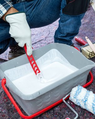 Koruyucu eldiven takan ellerin yakın çekimi. Bir ressam duvarı boyamak için beyaz boyayı hazırlar. İnşaat endüstrisi. İş Güvenliği.