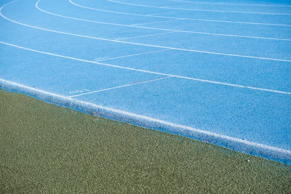 blue running track with race start marks next to grass