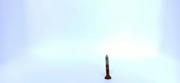 Beyaz arka planı olan ahşap bir masanın yüzeyindeki küçük bir vidanın yakın çekimi.