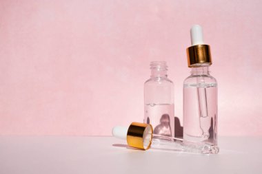 Pembe arka planda kozmetik sıvılı damlatıcı kavanozları. Yan görünüm, metin için boşluk.