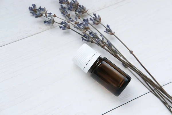 Bottle with lavender oil and dry lavender branches on a white wooden background. Side view, space for text.