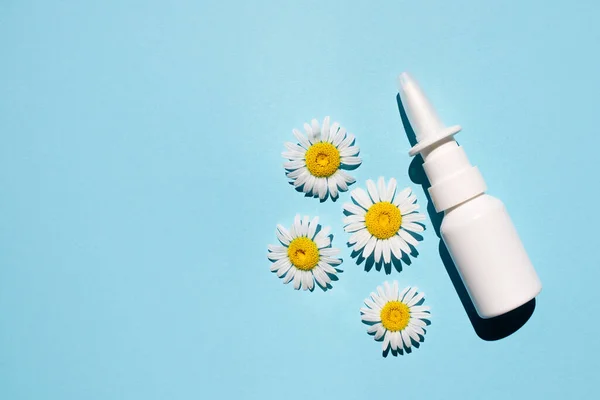 Nasal spray and natural chamomiles on a blue background. Flat lay, place for text.