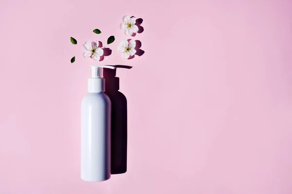 Mockup of a white empty body lotion bottle on a pink background and natural flowers. flat lay, place for text.