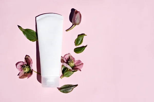 stock image Natural cosmetic cream in white tube, skin care mockup concept on pink background with natural hellebore flowers. a flat lay, place for text.