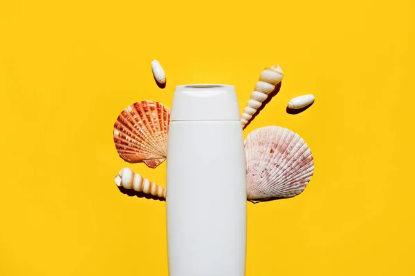Mockup of a white empty bottle of lotion from or for suntan with seashells on a yellow background. Flat lay, place for text.