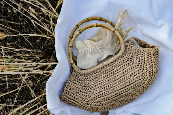 Handmade jute bag with bamboo handles on white canvas in a wheat field. View from above.
