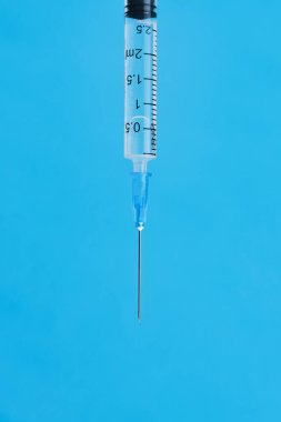 Metal iğneli ve mavi arka planlı tek kullanımlık şırınga. Dikey resim, metin için yer.
