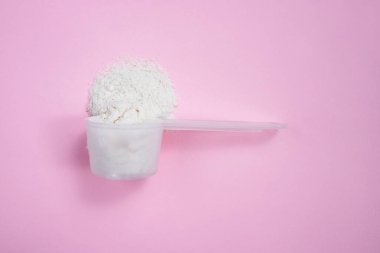 Pembe arka planda kolajen tozlu kaşık ölçüyorum. Yan görünüm, metin için boşluk.