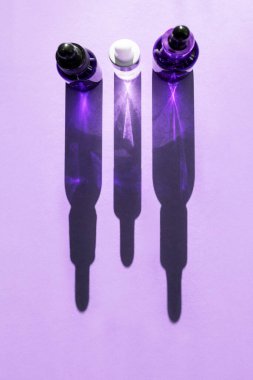 Mavi arka planda sıralanmış kozmetik sıvılarla dolu üç cam şişe, gölgeler. Dikey resim, üst görünüm.