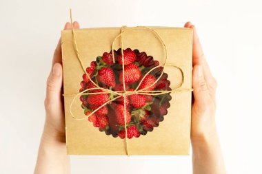 Beyaz arka planda taze çilek dolu el sanatları kutusunu tutan eller. Metin için yer.