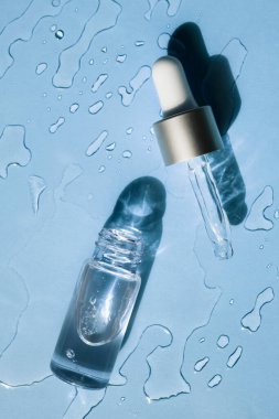 Glass bottle and pipette in a cosmetic transparent liquid on a blue background. Flat lay. clipart