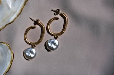 Büyük yuvarlak incili bej ipekli altın küpeler. Düz biçim, metin için boşluk.