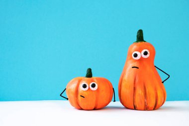 Komik yüzlü iki balkabağı, parlak mavi arka planda kabarık gözler ve ince saplar. Cadılar Bayramı partisi konsepti. Yan görünüm, metin için boşluk.
