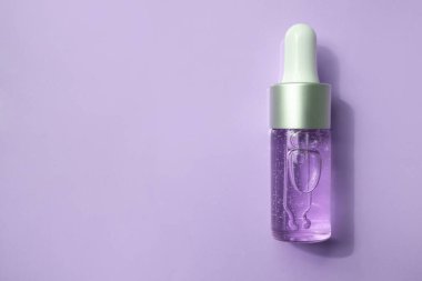 İçinde kozmetik sıvısı olan şeffaf bir damlacık şişesi mavi bir arka plana gölge düşürür. Yaklaş, düz yat..