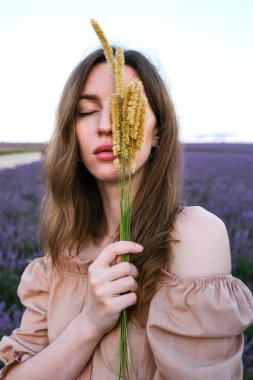 Doğada yürürken kabarık çimen saplarını tutan güzel genç bir kadın..