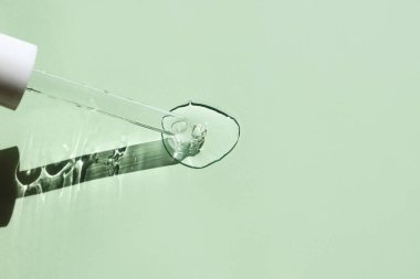 Bir damla aloe vera jeli ve yeşil arka planda cam bir pipet..