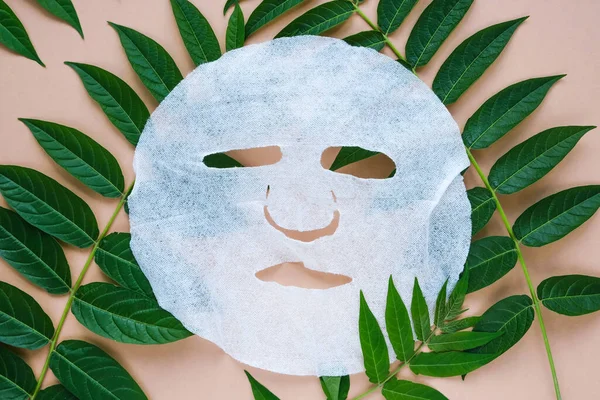 Fabric cosmetic face mask on green natural leaves. Spa treatments for skin care. Flat lay.