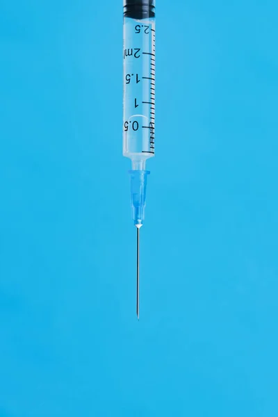 Disposable syringe with a metal needle and on a blue background. Vertical image, place for text.