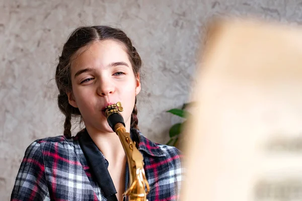 The girl learns to play the saxophone. The child is studying music at home.