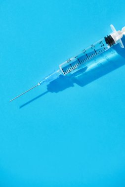 Temiz iğneyle tek kullanımlık şırınga ve parlak mavi arka plana yerleştirilmiş sıvı ilaç. Düz, dikey resim.