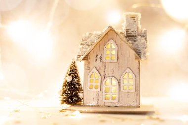 Işıklı arka planda bir oyuncak ev. Noel ve Yeni Yıl için aksesuarlar.