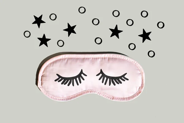 Pink sleep mask with eyelashes on a gray background with black stars. Healthy sleep concept. Space for text,top view.