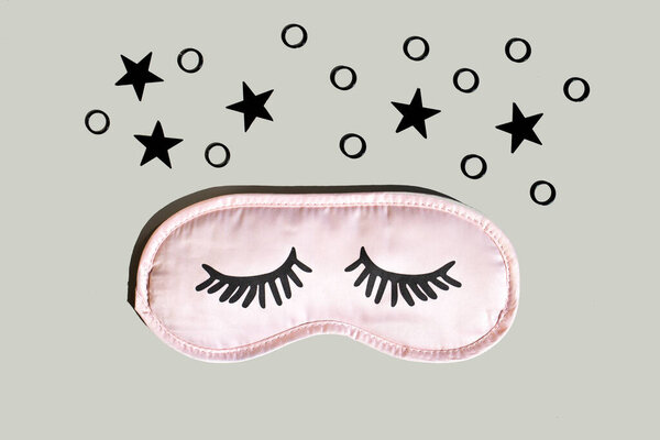 Pink sleep mask with eyelashes on a gray background with black stars. Healthy sleep concept. Space for text,top view.