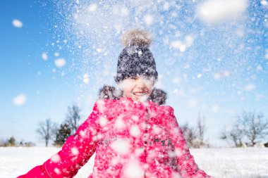 Mutlu kız güneşli bir kış gününde gökyüzüne kar atıyor..