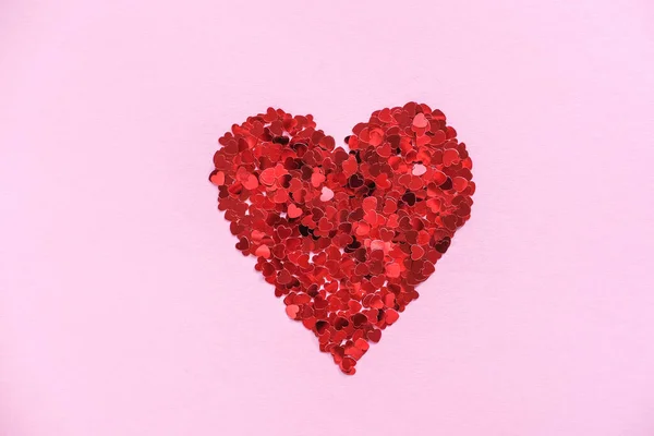 stock image Heart made of shiny red small decorative hearts on a pink background. Flat lay, place for text. Festive minimal composition.