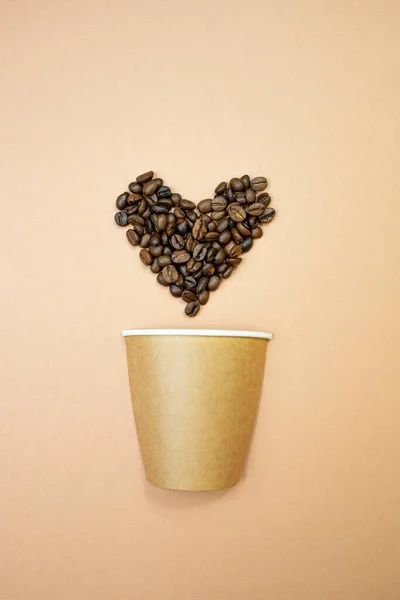 Natural reusable paper cup and heart shaped coffee beans on a beige background. Zero Waste Lifestyle. Flat lay, vertical image.