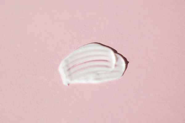 A smear of white moisturizer on a pink background. Flat lay, close-up.