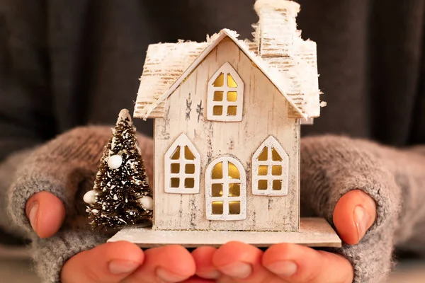 stock image A woman's hands hold a Christmas decoration in the form of a house in which the lights are on.