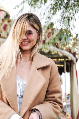 Şehirde yürüyen bej ceketli çekici bir sarışın. Dikey resim.