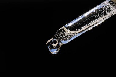 Kozmetik sıvılı cam pipet ya da siyah zemin üzerinde hava kabarcıkları olan poliglutamik asit. Yan görünüm, yakın plan.