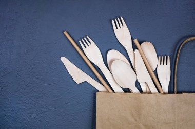 Tek kullanımlık bambu çatal bıçak takımı gri bir arka planda kağıt bir torba içinde. Düz yatıyordu.