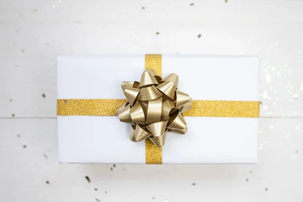 Gift box in white paper and with gold bow on white background. Top view.