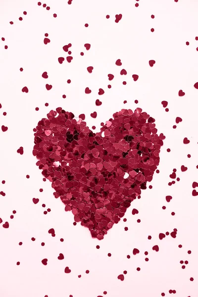 stock image Valentine's day background. Heart made of shiny red small decorative hearts on a pink background strewn with sparkles. Demonstrating the colors of 2023 Viva Magenta. Vertical image, flat lay.