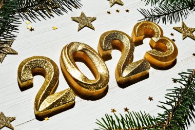 Tatil geçmişi. Mutlu yıllar 2023. Beyaz ahşap bir zemin üzerinde altın parıldayan numaralar 2023 ladin dalları ve parıldayan yıldızlarla. Yan görünüm, yakın plan.