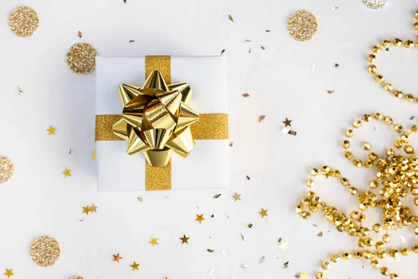 Box with a gold bow on a white background among sparkles and candy. Top view, place for text. New Year\'s composition.