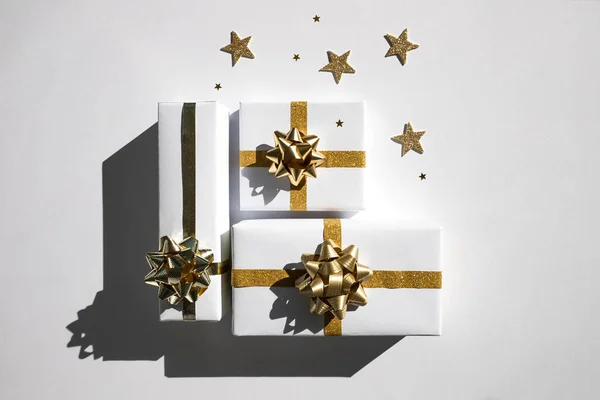 White paper gift boxes with a gold bow on a white background with sequins cast a shadow. A concept for Christmas and New Year\'s Eve celebrations. Flat lay, top view, copy space.