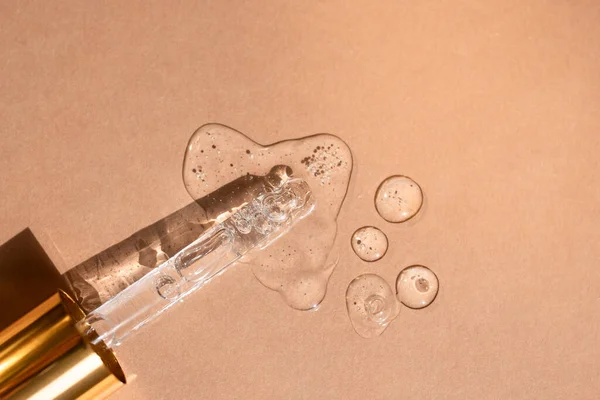 Serum drops with air bubbles and glass pipette on beige background. Flat lay, top view, copy space.