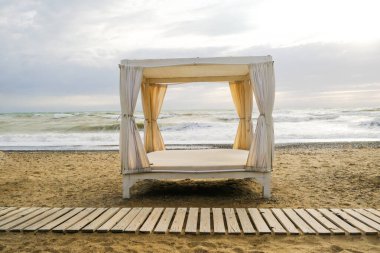 Beach tent with fabric curtains on the beach against a blue sky background.