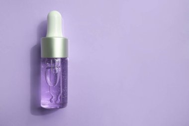 İçinde kozmetik sıvısı olan şeffaf bir damlacık şişesi mavi bir arka plana gölge düşürür. Yaklaş, düz yat..