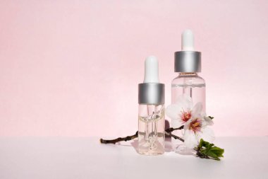 Dropper jars with cosmetic liquid and natural flowering branch on a pink background. Side view, space for text.